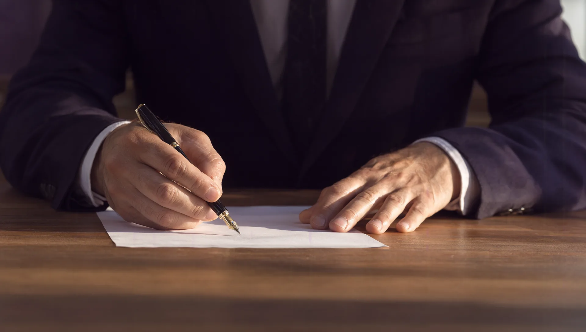 Primo piano delle mani di un uomo d'affari che firma un contratto con la stilografica su una scrivania di legno.