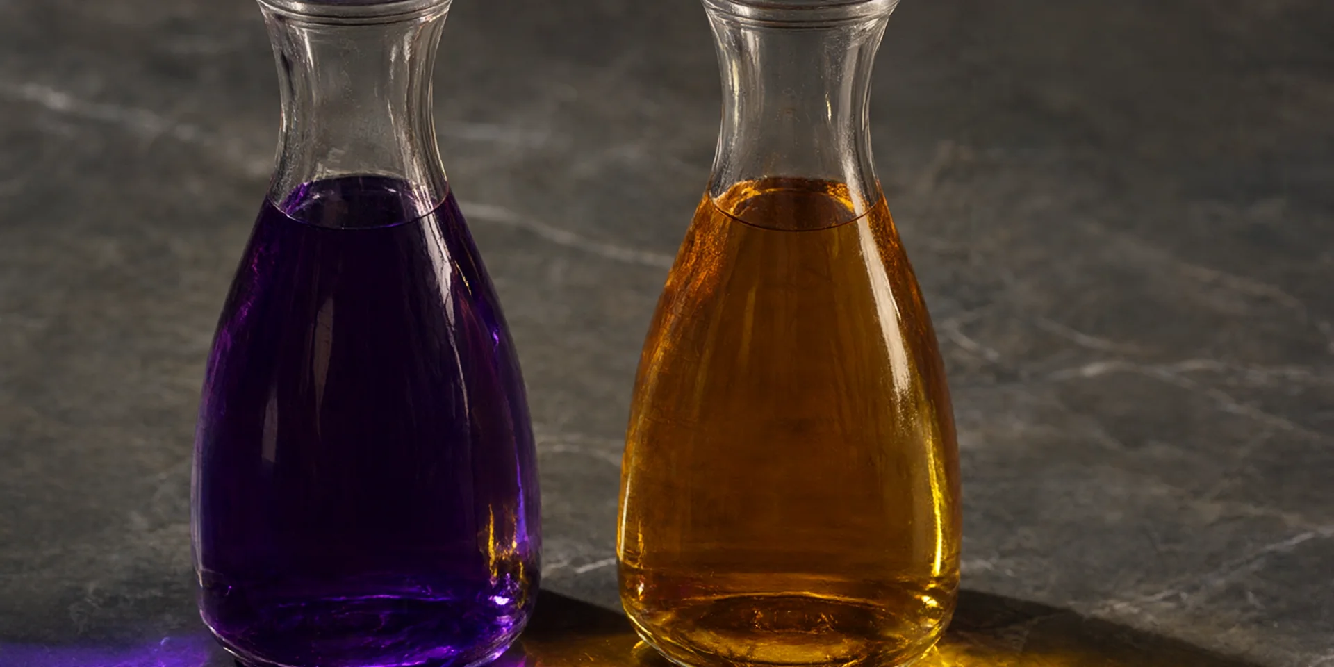 Due caraffe di vetro identiche, fianco a fianco: una con un liquido viola, l'altra con un liquido ambrato.