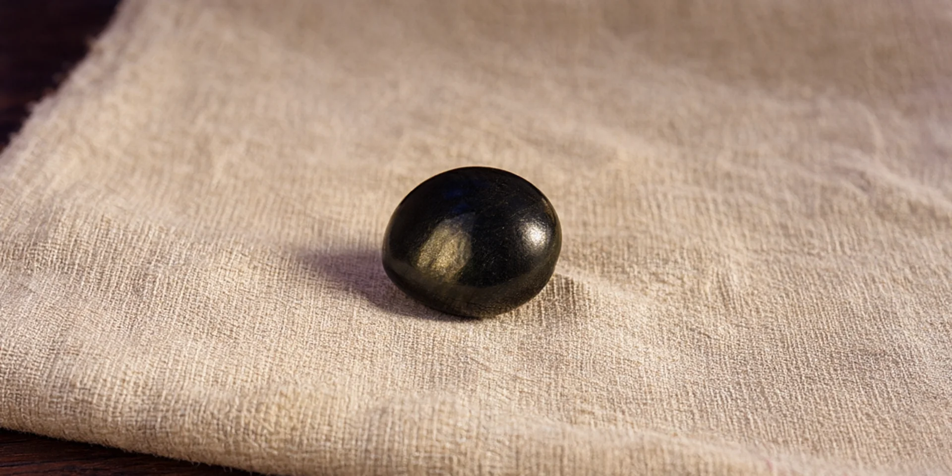Una pequeña piedra de obsidiana pulida sobre un trozo de lino crudo crema sobre una mesa de roble oscuro.