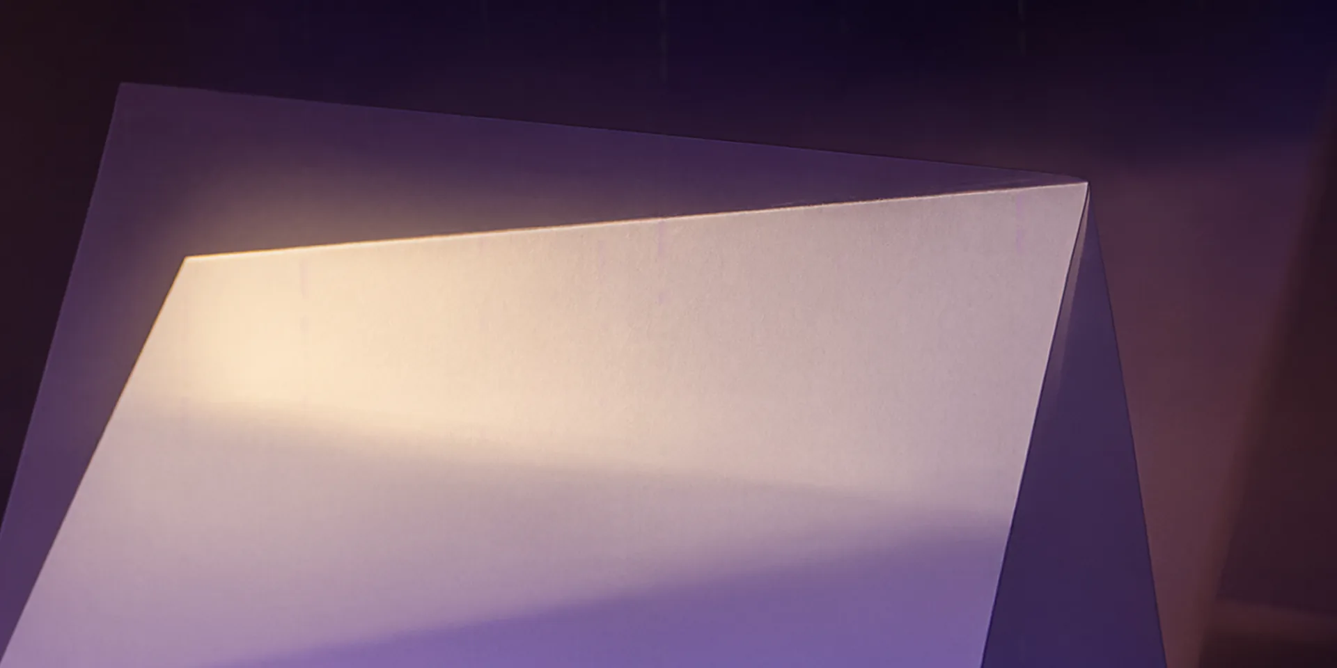 Una hoja de papel blanco en pie sobre una superficie oscura con un haz de luz cálida iluminando solo el tercio superior mientras el resto cae en sombra profunda.